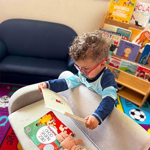 Child reading a book in a cozy classroom with colorful books and a blue chair nearby