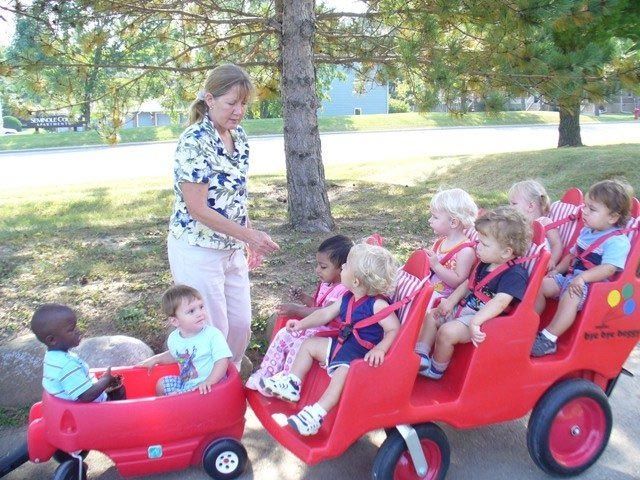 Teacher loading children into a red wagon train in a park