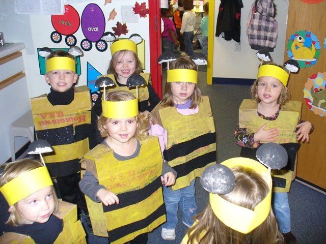 Children wearing yellow-and-black bee costumes and headbands stand in a classroom.