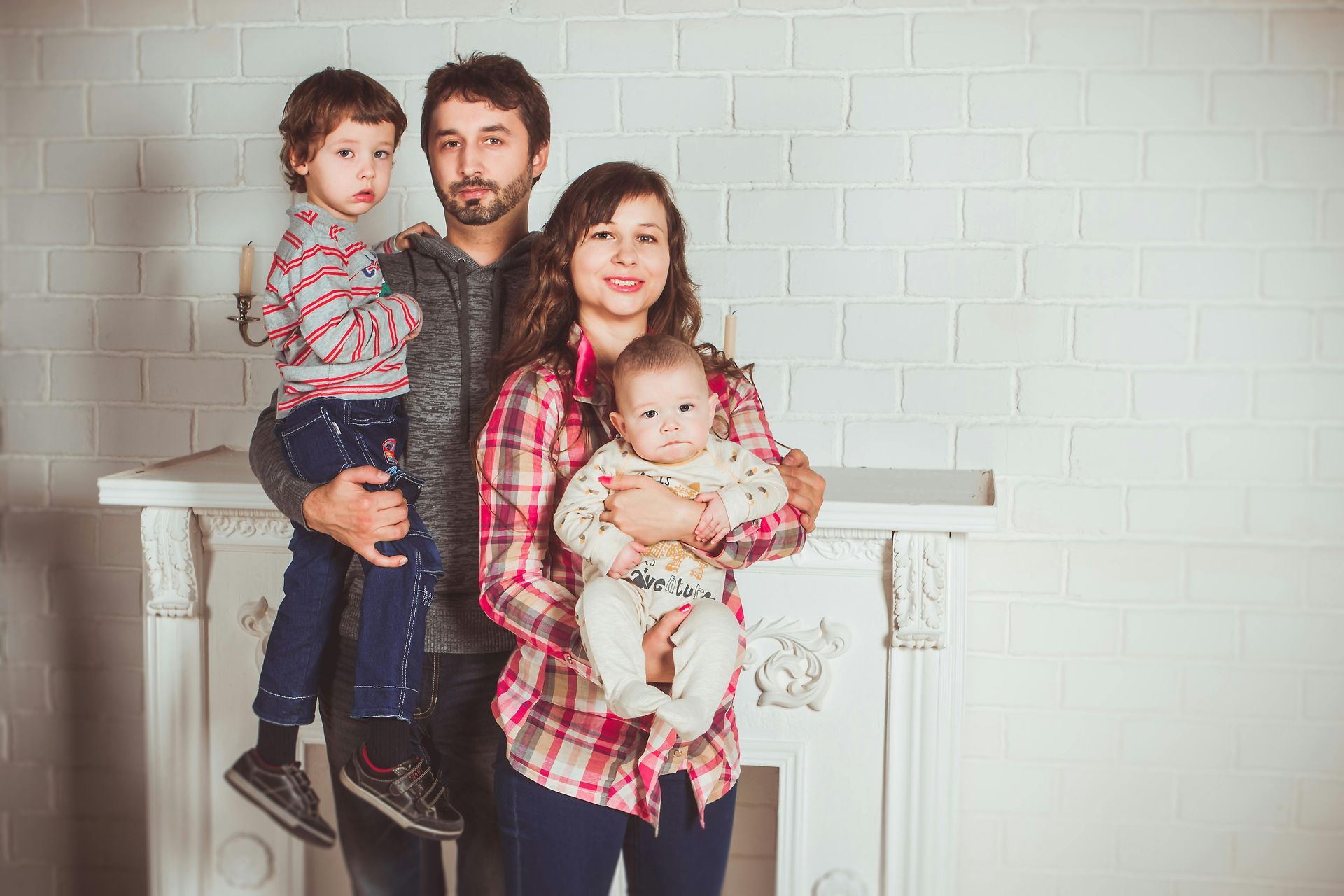Family of four poses in front of a white brick wall and fireplace.