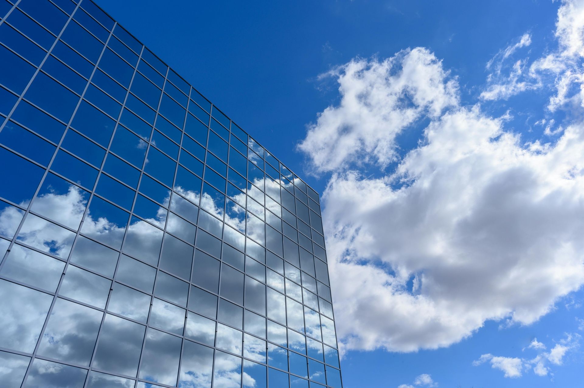 Glass skyscraper reflecting bright blue sky and puffy white clouds.
