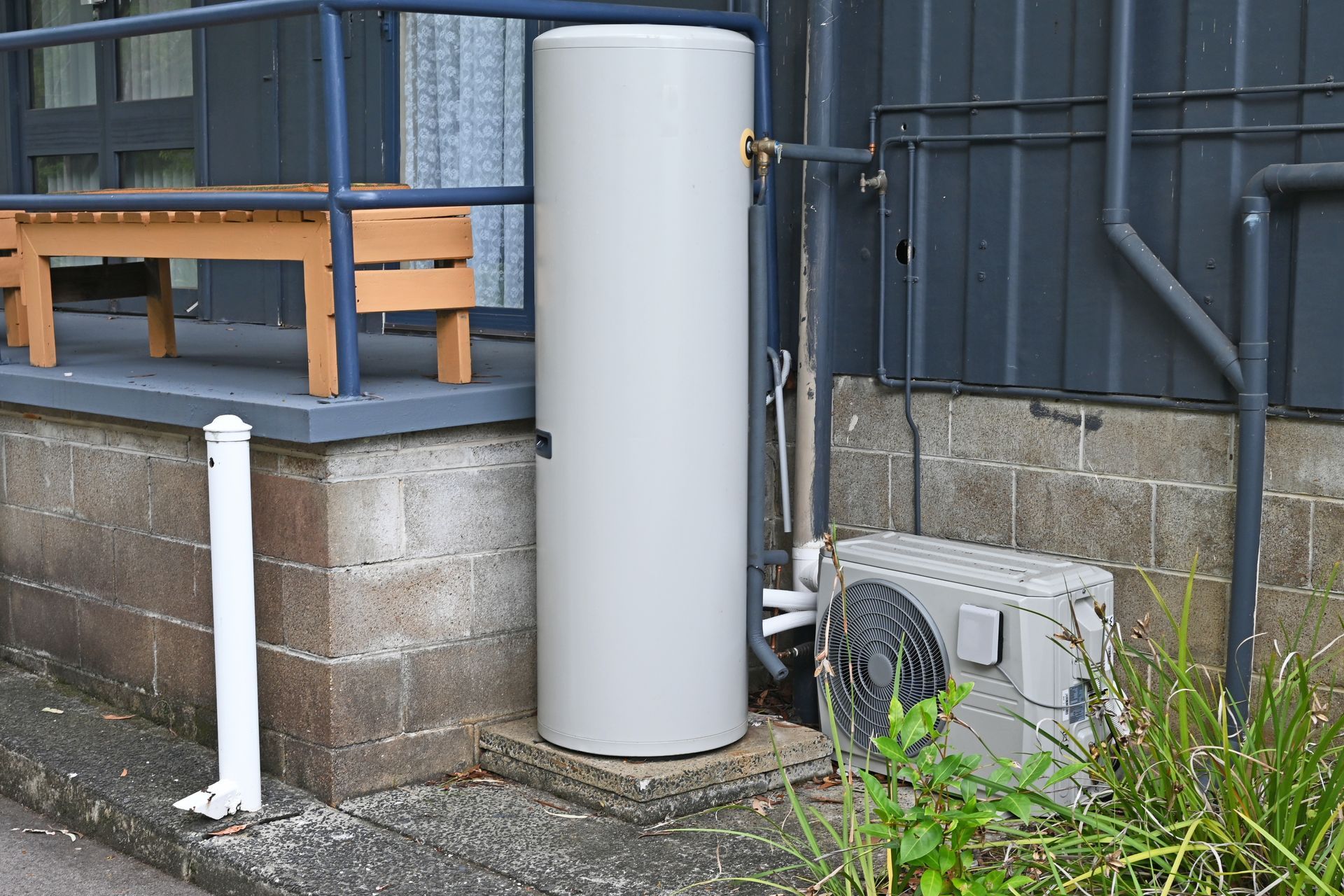 Tall, Hot Water Tank Next to an Air Conditioning Unit and a Building — Mazlin Electrical Services Pty Ltd in Annandale, QLD