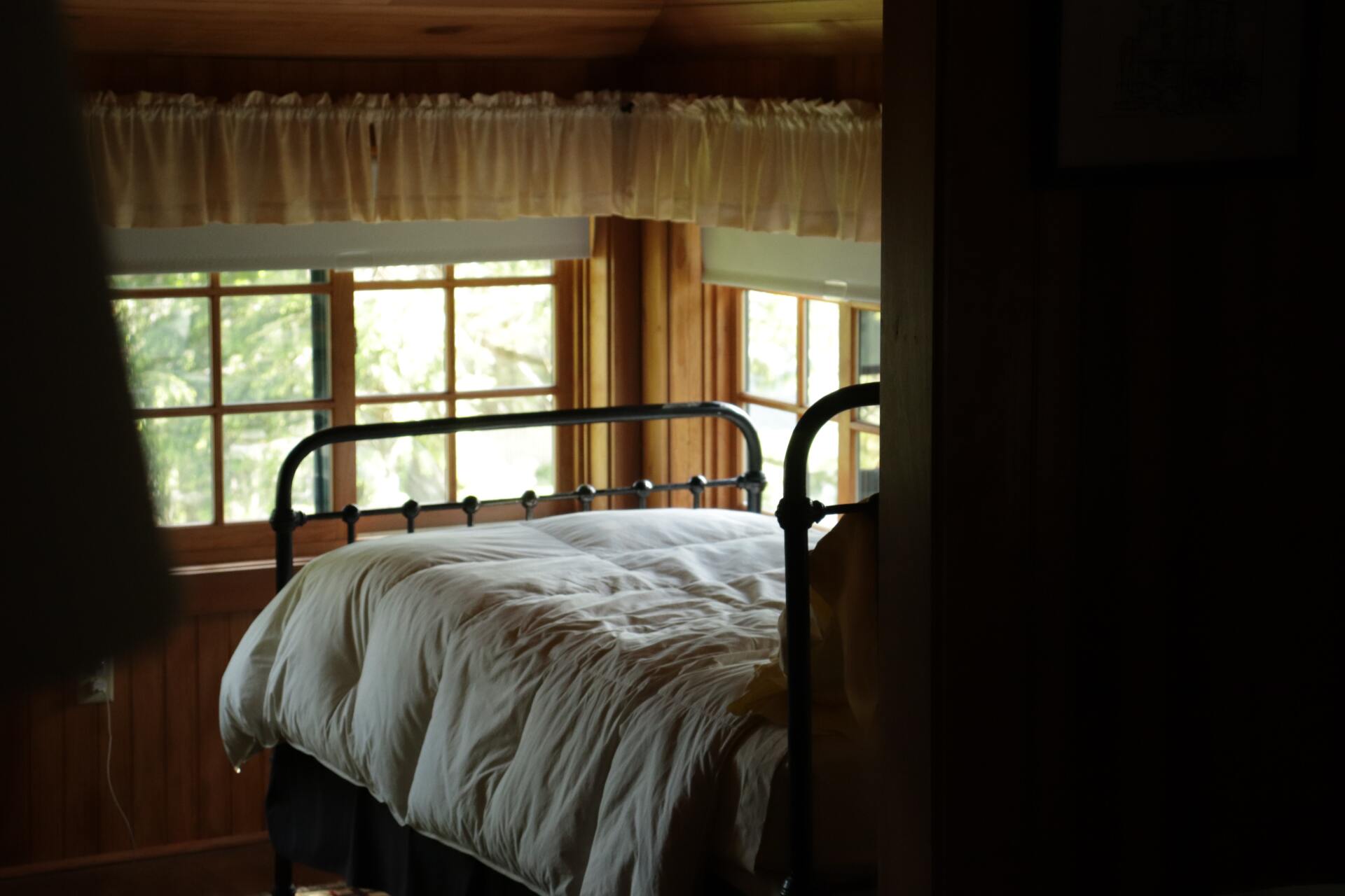 Habitación acogedora con cama de metal, ropa de cama blanca y ventana soleada con cortinas.