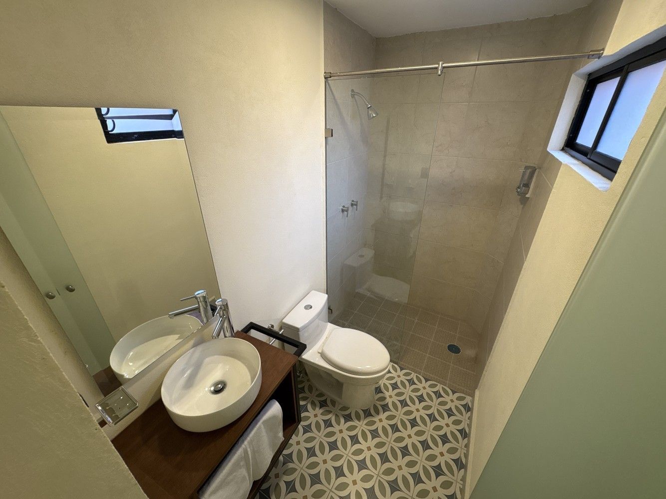 Baño pequeño con inodoro, lavabo con mueble, cabina de ducha y baldosas estampadas en el suelo.
