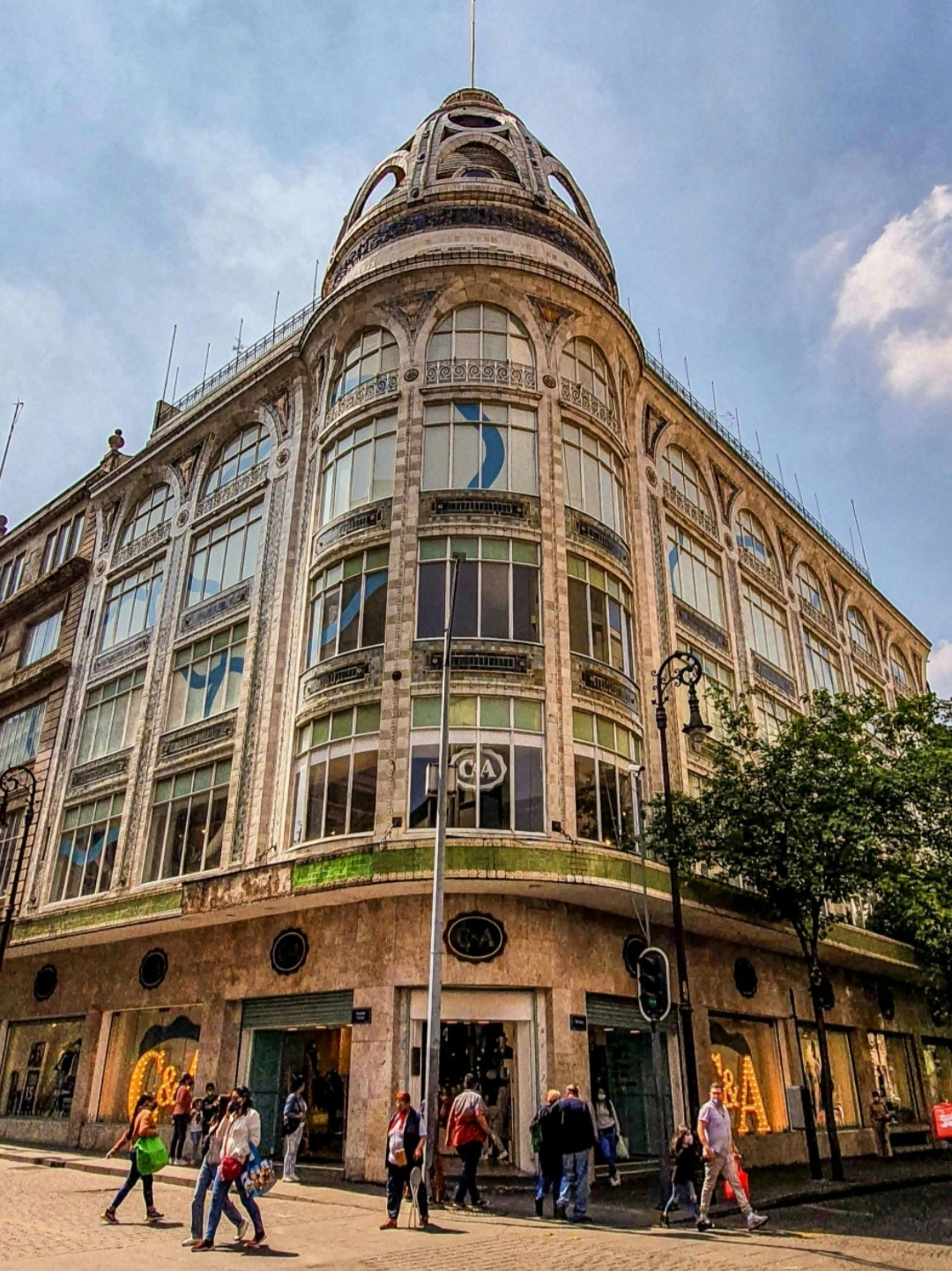 Vista de una esquina de un edificio histórico de varias plantas con una fachada ornamentada y gente caminando por la acera.