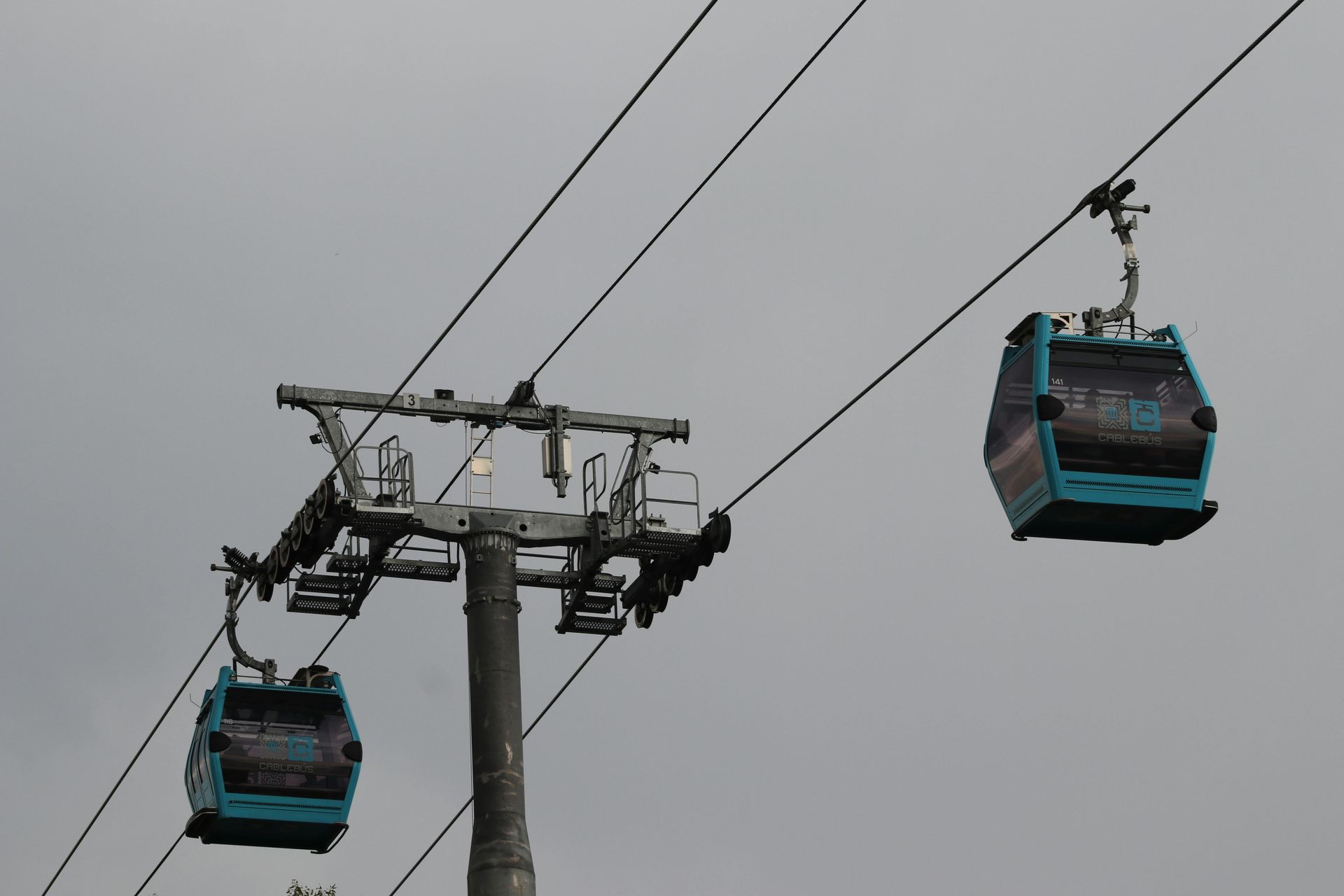 Dos teleféricos de color turquesa suspendidos en un telesilla contra un cielo gris