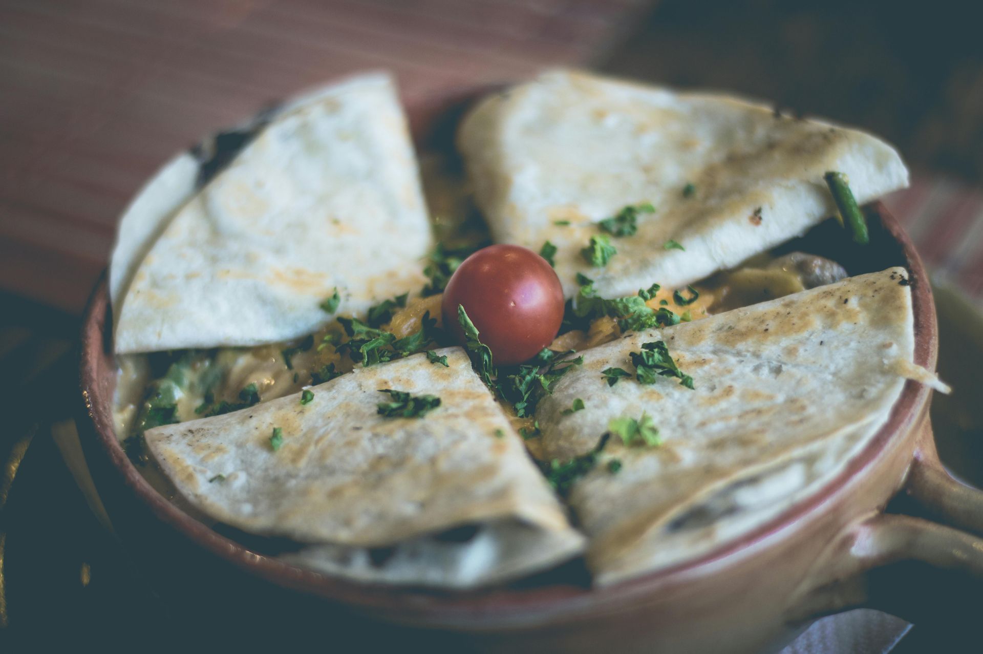 Plato de trozos de quesadilla cubiertos con hierbas y un tomate cherry sobre una mesa de madera.