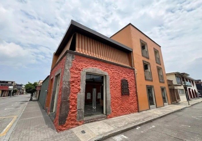 Esquina de un edificio moderno de ladrillo rojo y color canela en una calle pavimentada bajo un cielo nublado.