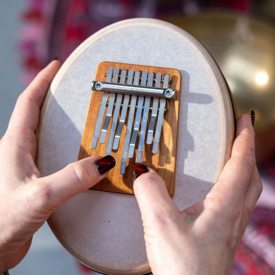 Handen die een kalimba vasthouden, een houten muziekinstrument met metalen tanden. De nagels zijn rood geverfd.