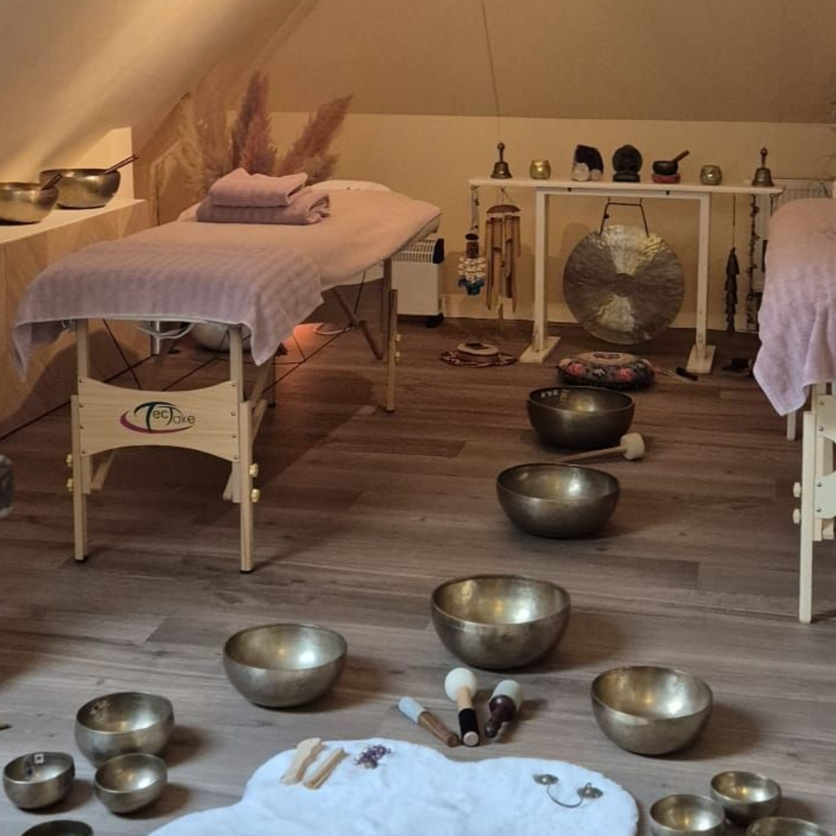 Een ruimte voor klanktherapie met massagetafels, klankschalen, een gong en decoratieve objecten.