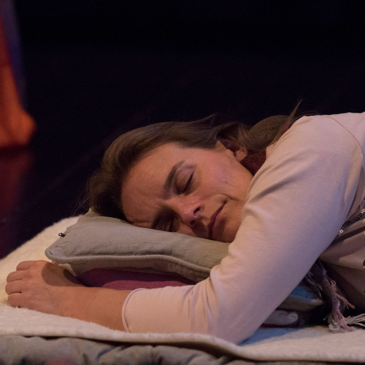 Vrouw ligt op een kussen en deken naast een klankschaal, mogelijk aan het mediteren of slapen.