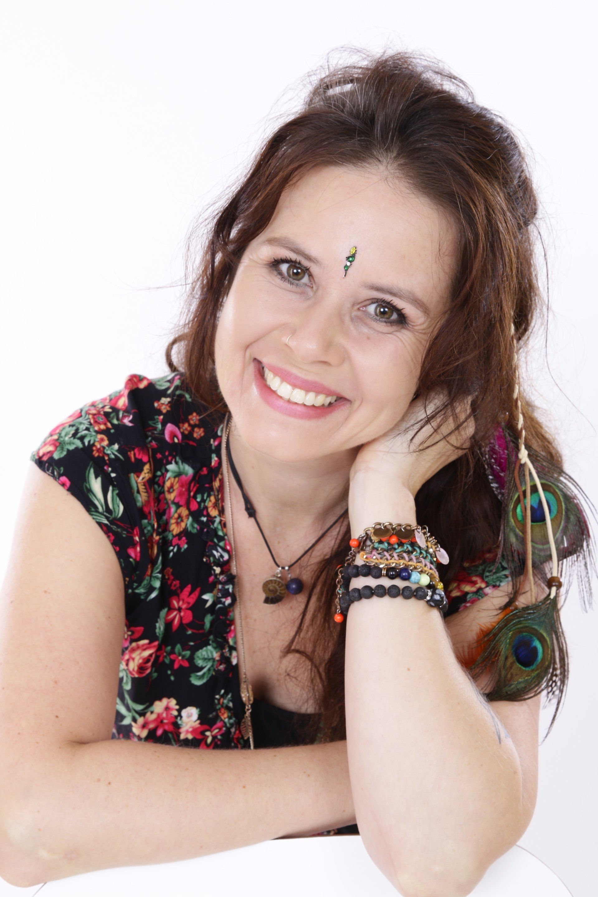 Vrouw met bruin haar lacht, draagt ​​een top met bloemenprint, sieraden en een bindi; oorbellen met pauwenveren.