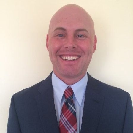 A bald man in a suit and tie smiles for the camera