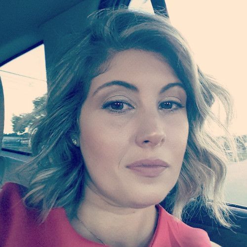 A woman in a red shirt is sitting in the back seat of a car.