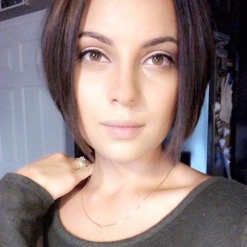 A woman with short hair is taking a selfie with her hand on her shoulder.