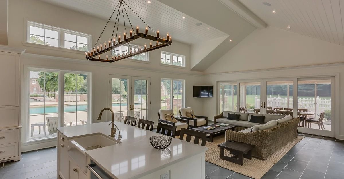 Bright open-plan living room and kitchen with white walls, large windows, gray tile, and modern furniture.