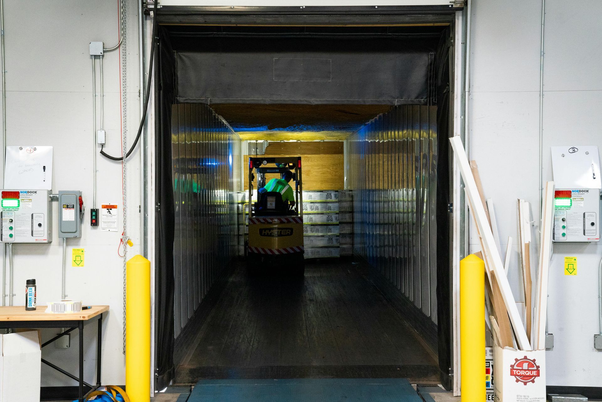 A warehouse worker in a blue shirt and tan pants inspects a pallet of goods wrapped in plastic inside a warehouse.