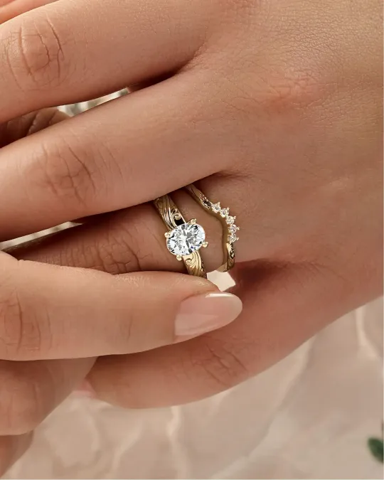 Hands wearing a gold ring with a round diamond on a soft beige background