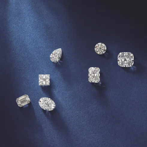 Six diamond rings and earrings arranged on a dark blue satin background