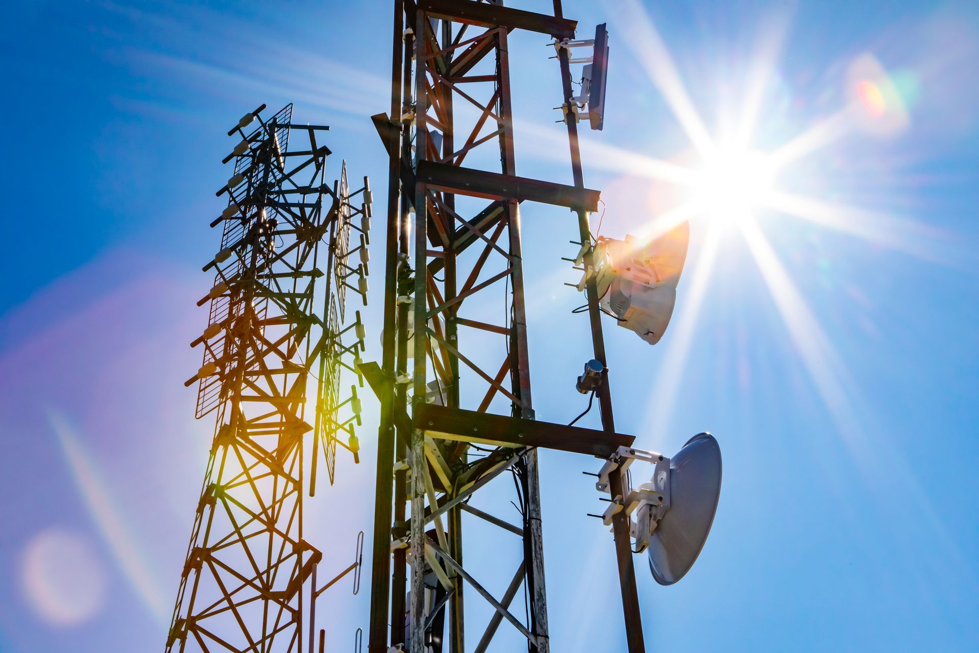 The sun is shining through the antennas of a telephone tower.
