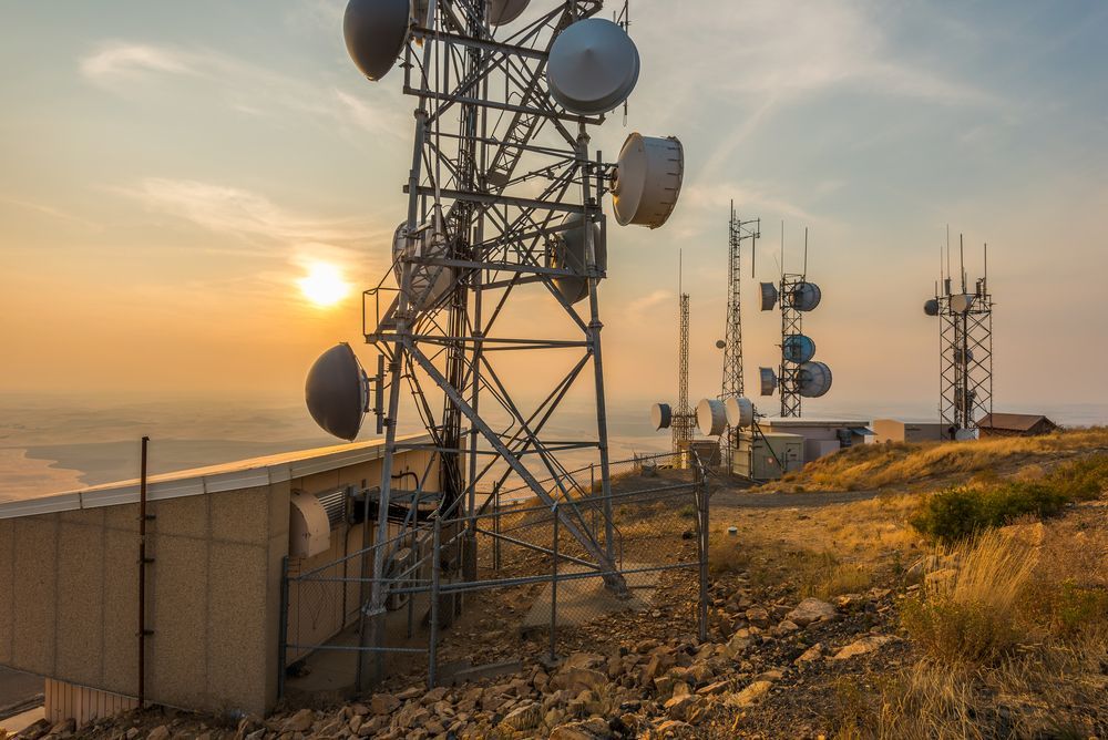 A group of antennas sitting on top of a hill at sunset.