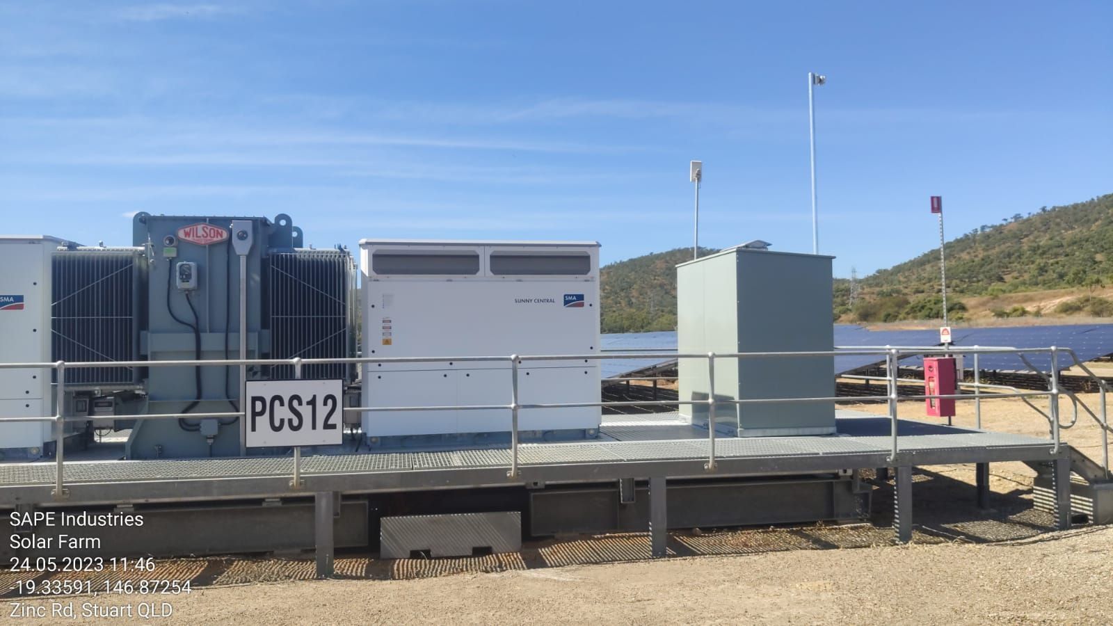 A large transformer is sitting on top of a metal platform next to a solar panel.