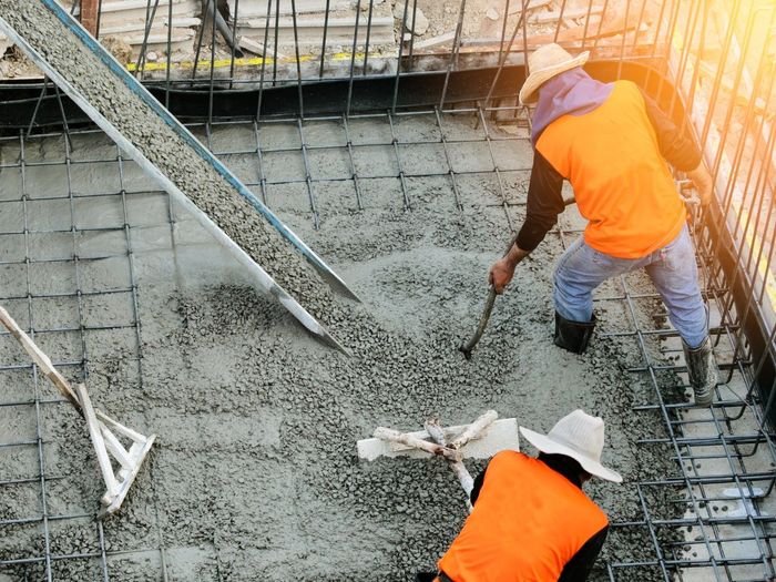 Construction workers pouring and leveling concrete into a reinforced foundation.