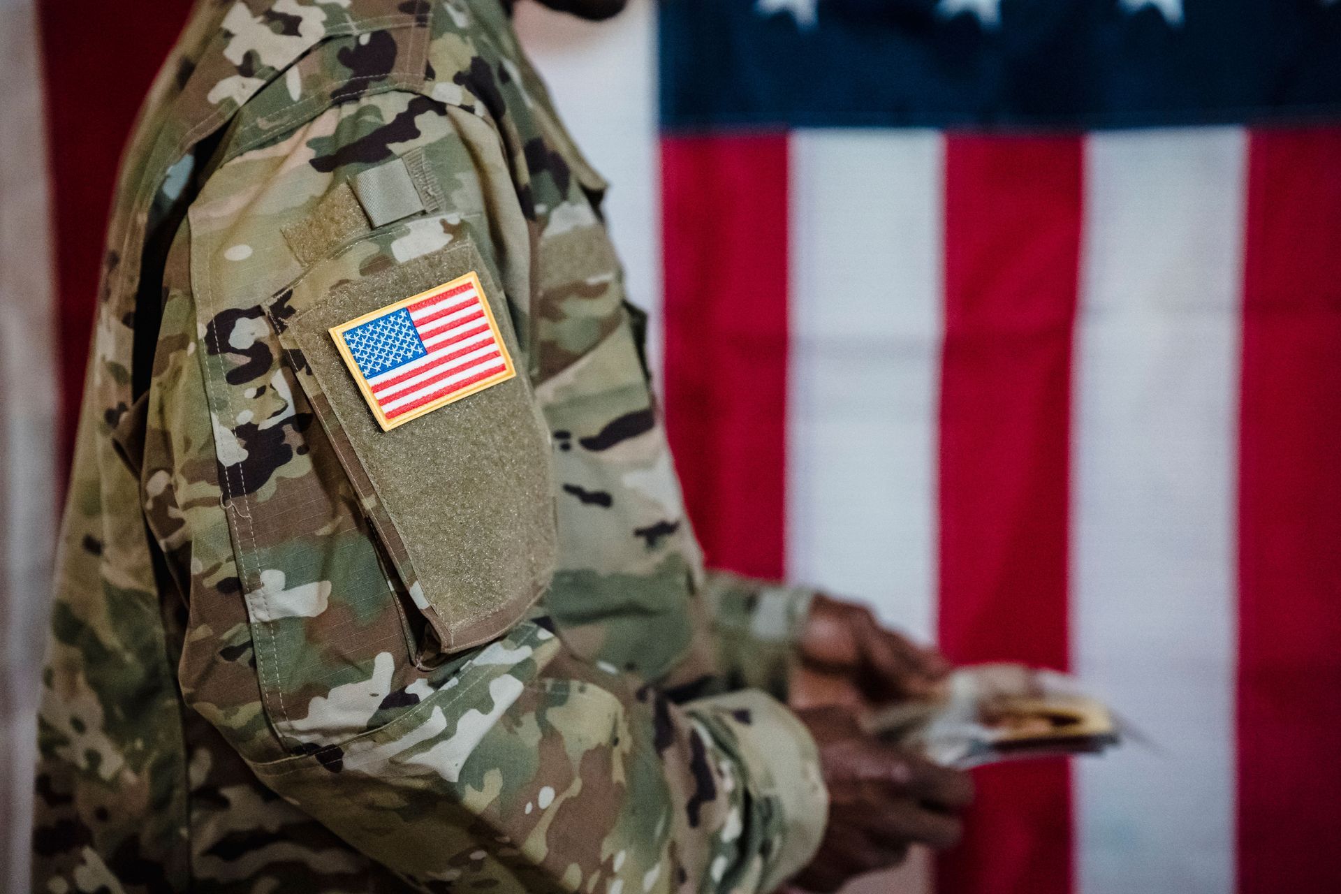 picture of a man in camo standing in front of an american flag.