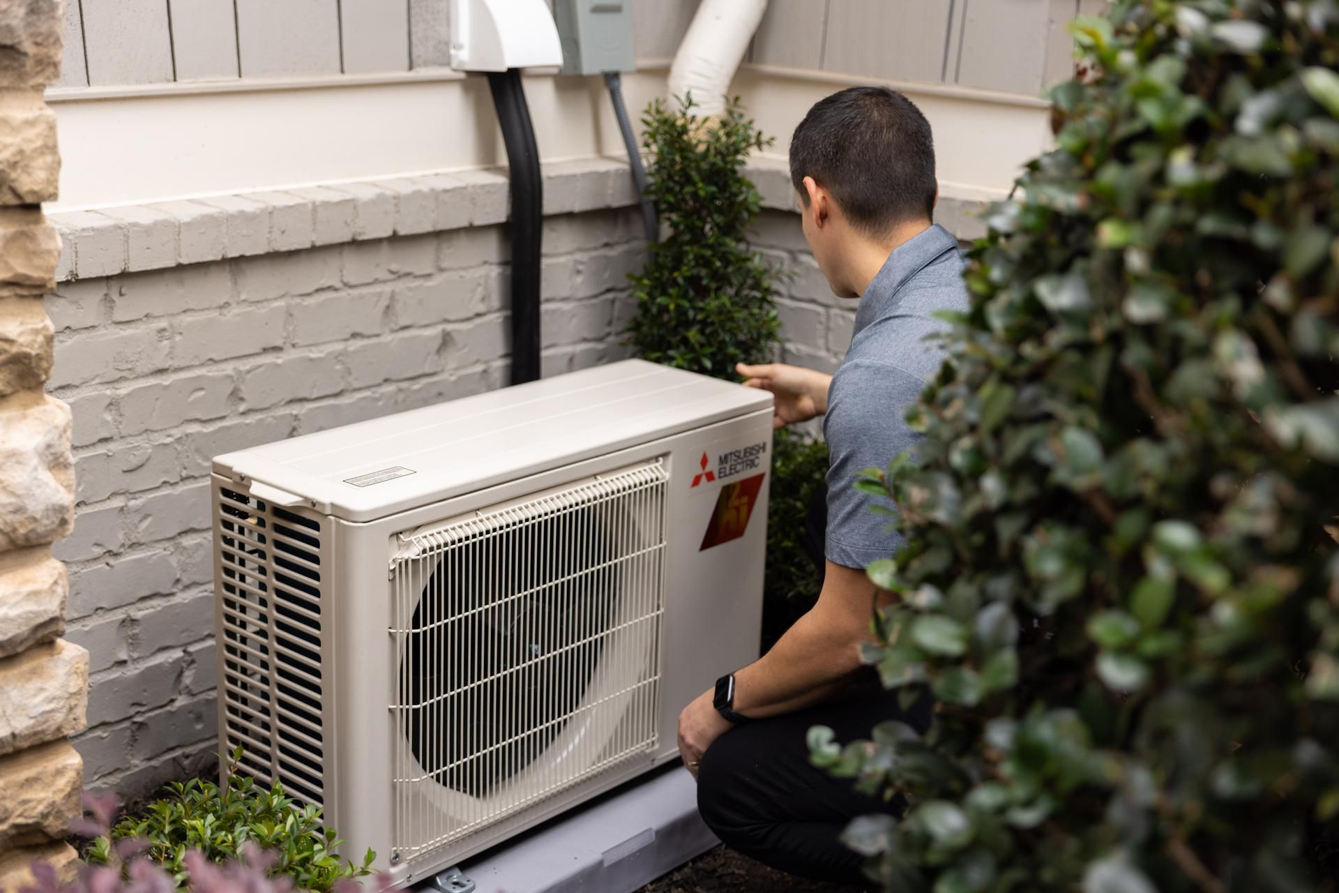 A person inspecting an outdoor heat pump unit next to a building.
