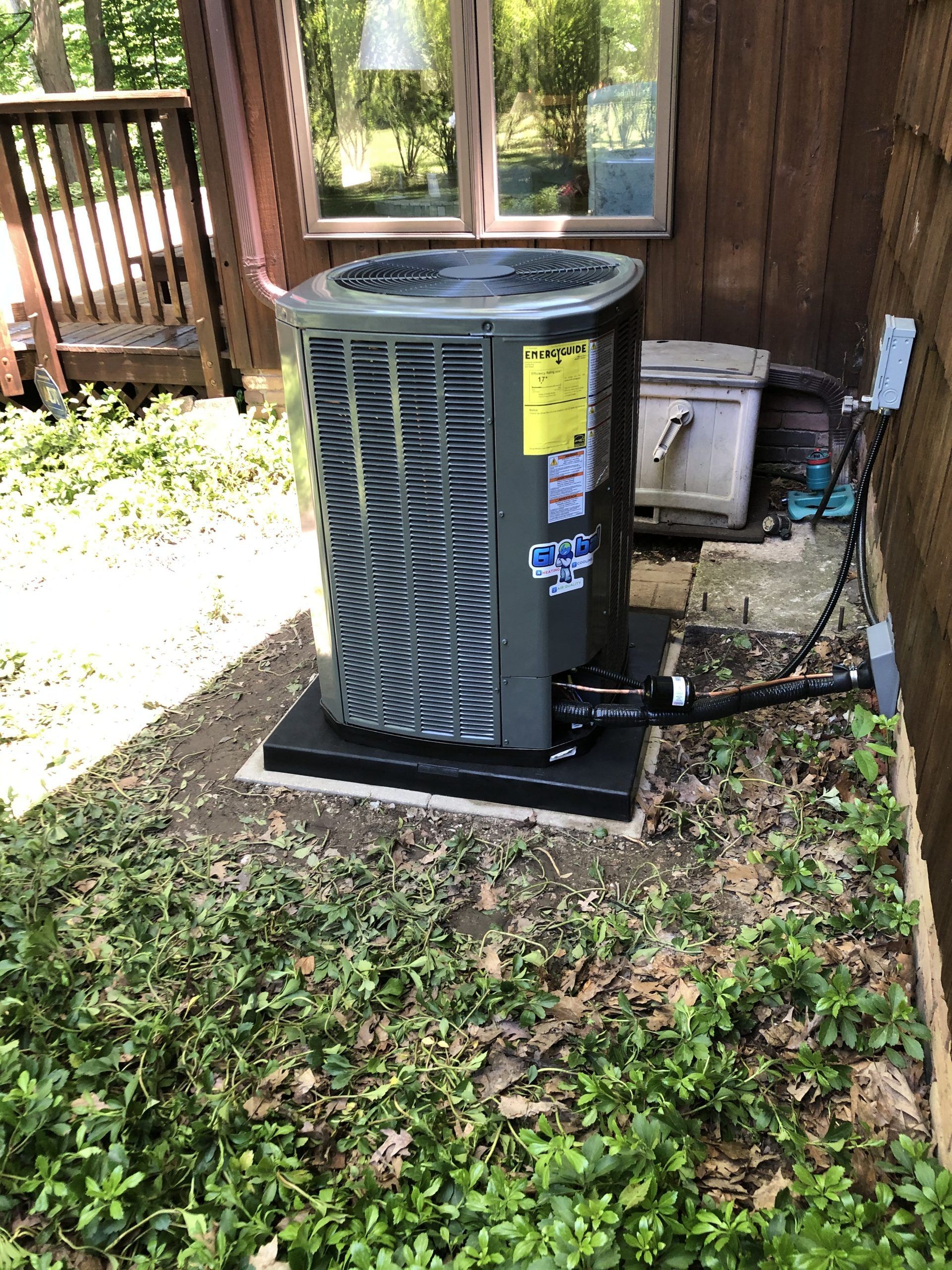 Air conditioning unit outside a building, set on a black base amidst greenery.