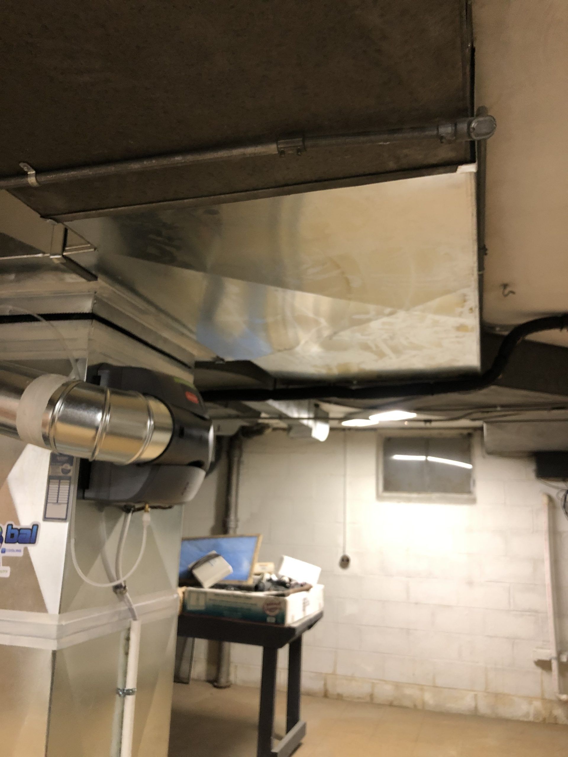 Metal HVAC ductwork installed on a basement ceiling. Conduit and wires also visible.