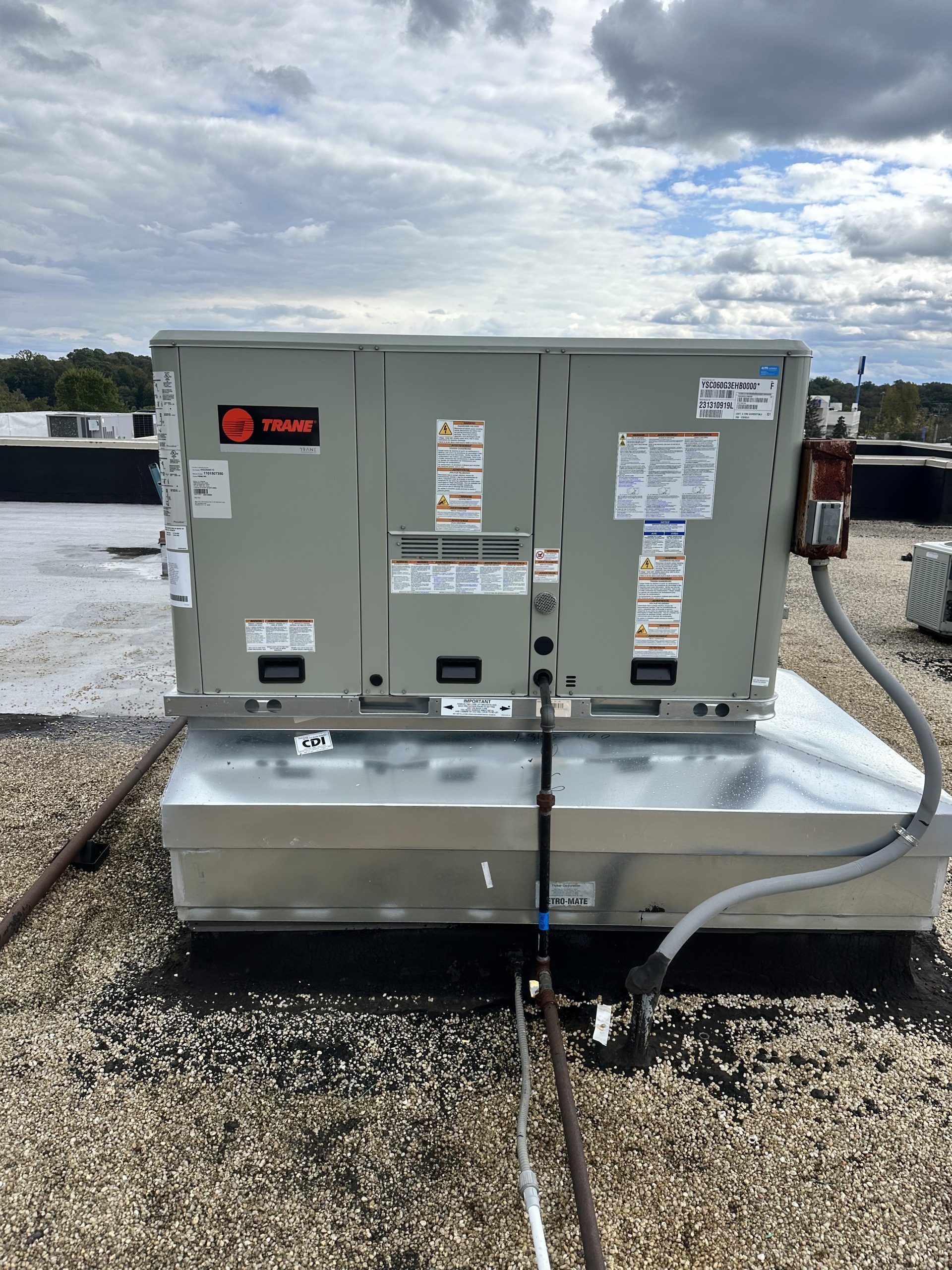 Rooftop HVAC unit, Trane brand, silver and gray, mounted on a metal base, on a gravel-covered flat roof.