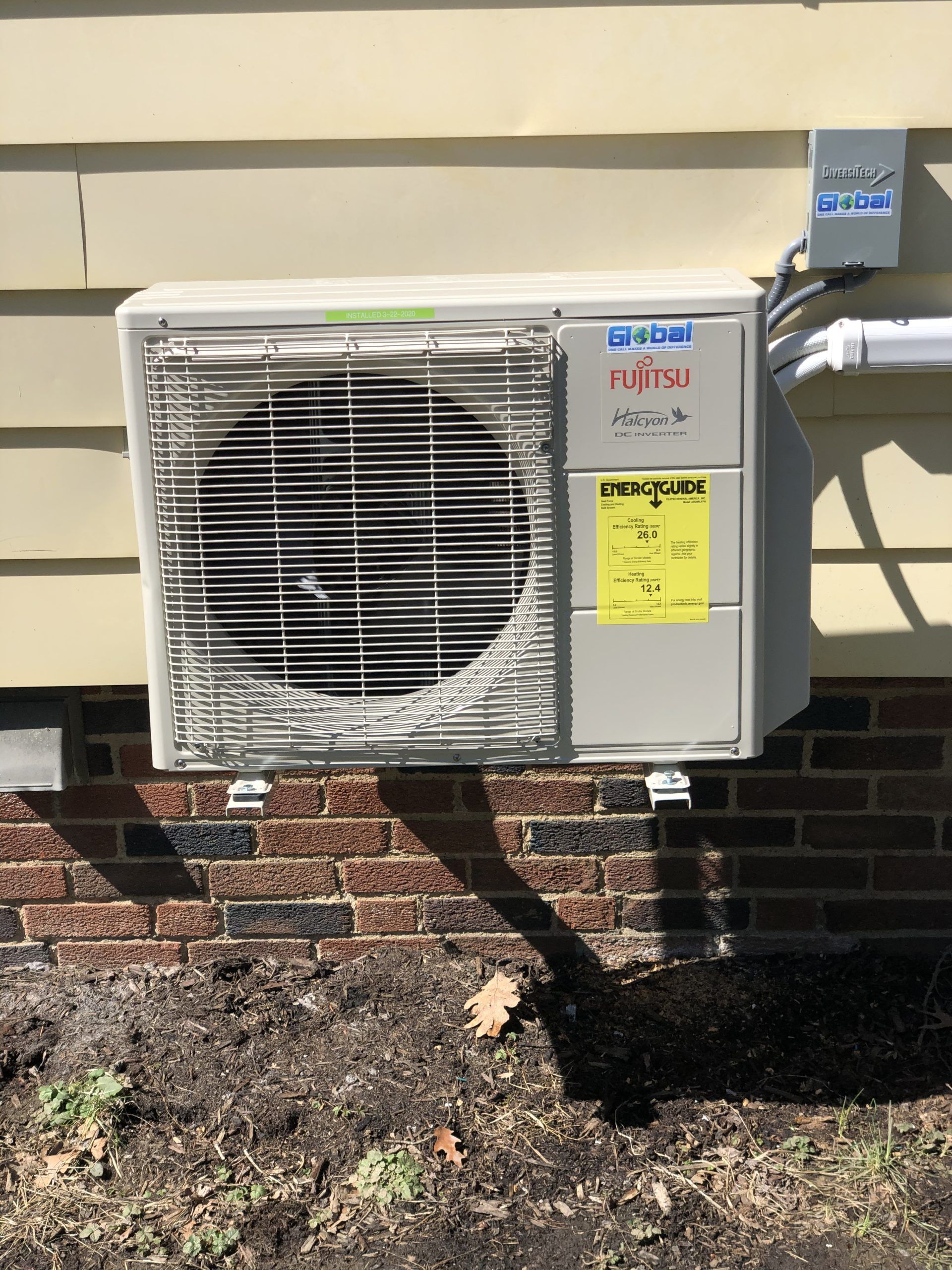 Fujitsu heat pump mounted on a brick and siding wall.
