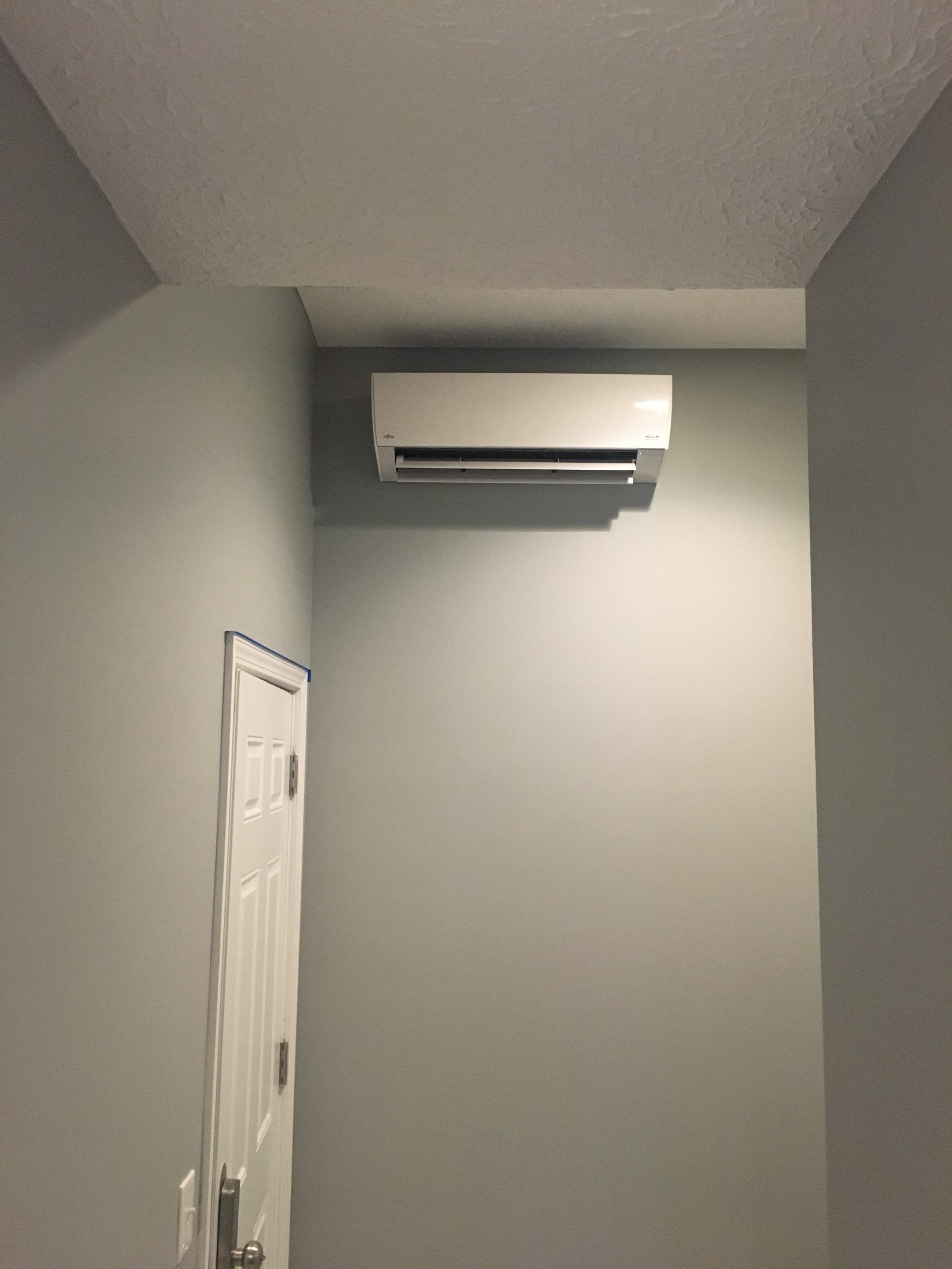 White air conditioning unit mounted on a gray wall above a white door.