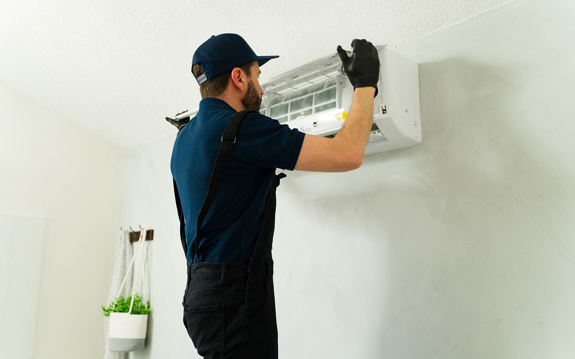 Man in uniform installing wall-mounted air conditioner on a white wall.