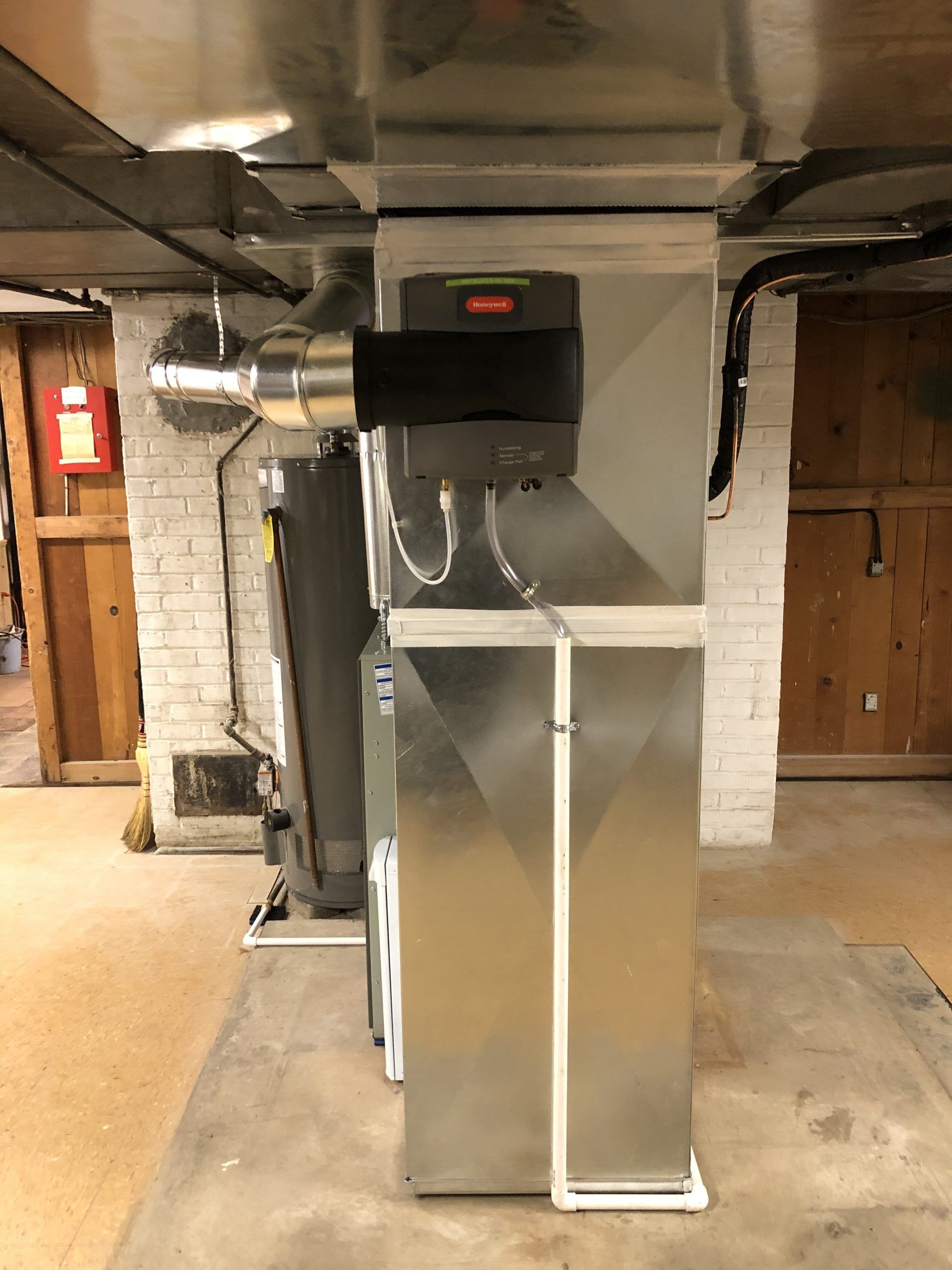 A furnace and humidifier system in a basement setting, silver metal finish, with attached water lines.