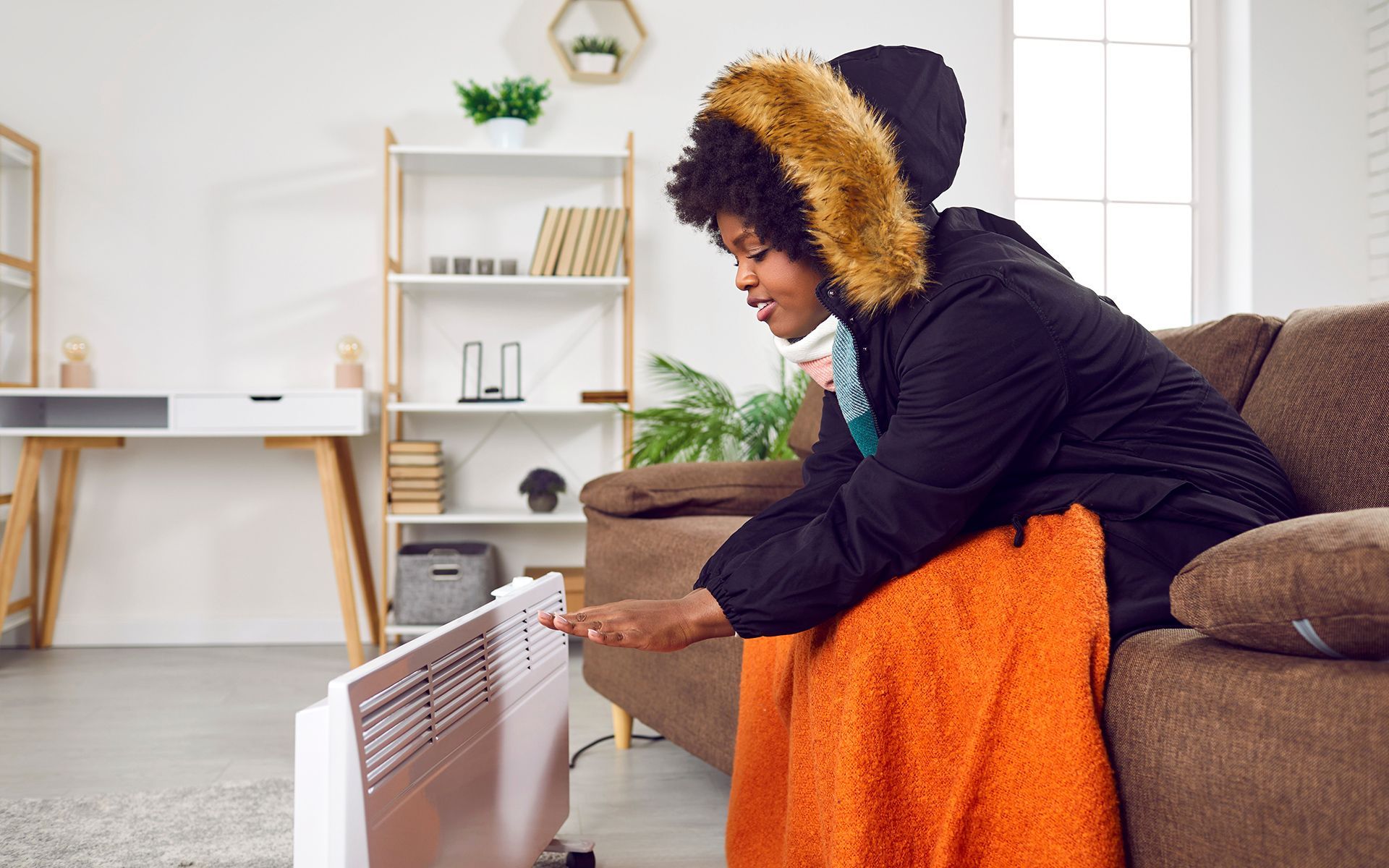 Person wearing coat, adjusting space heater in a cold living room.