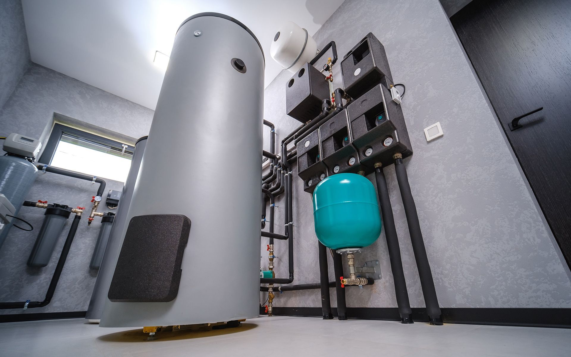Plumbing room with a water heater, a blue expansion tank, and pipes against a gray wall.