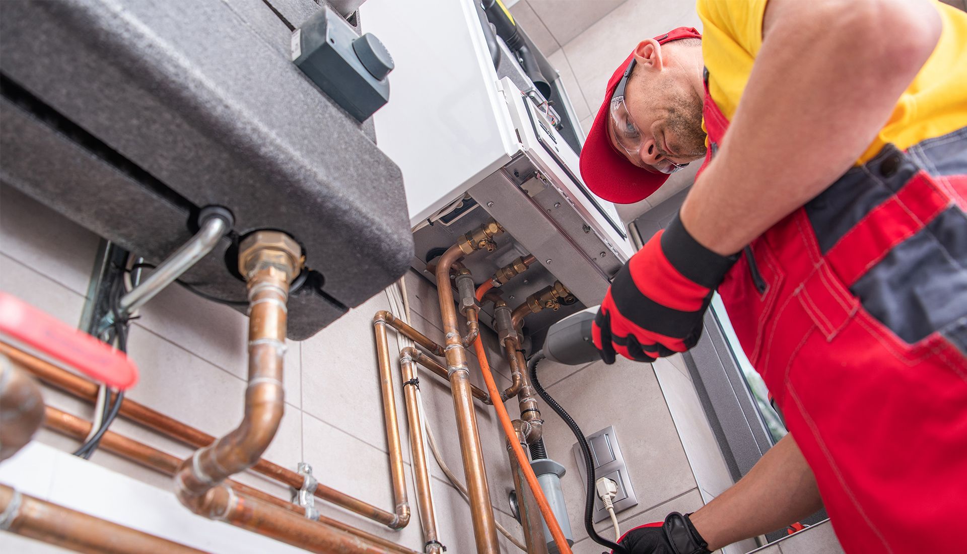 A person in red overalls and gloves working on heating pipes.