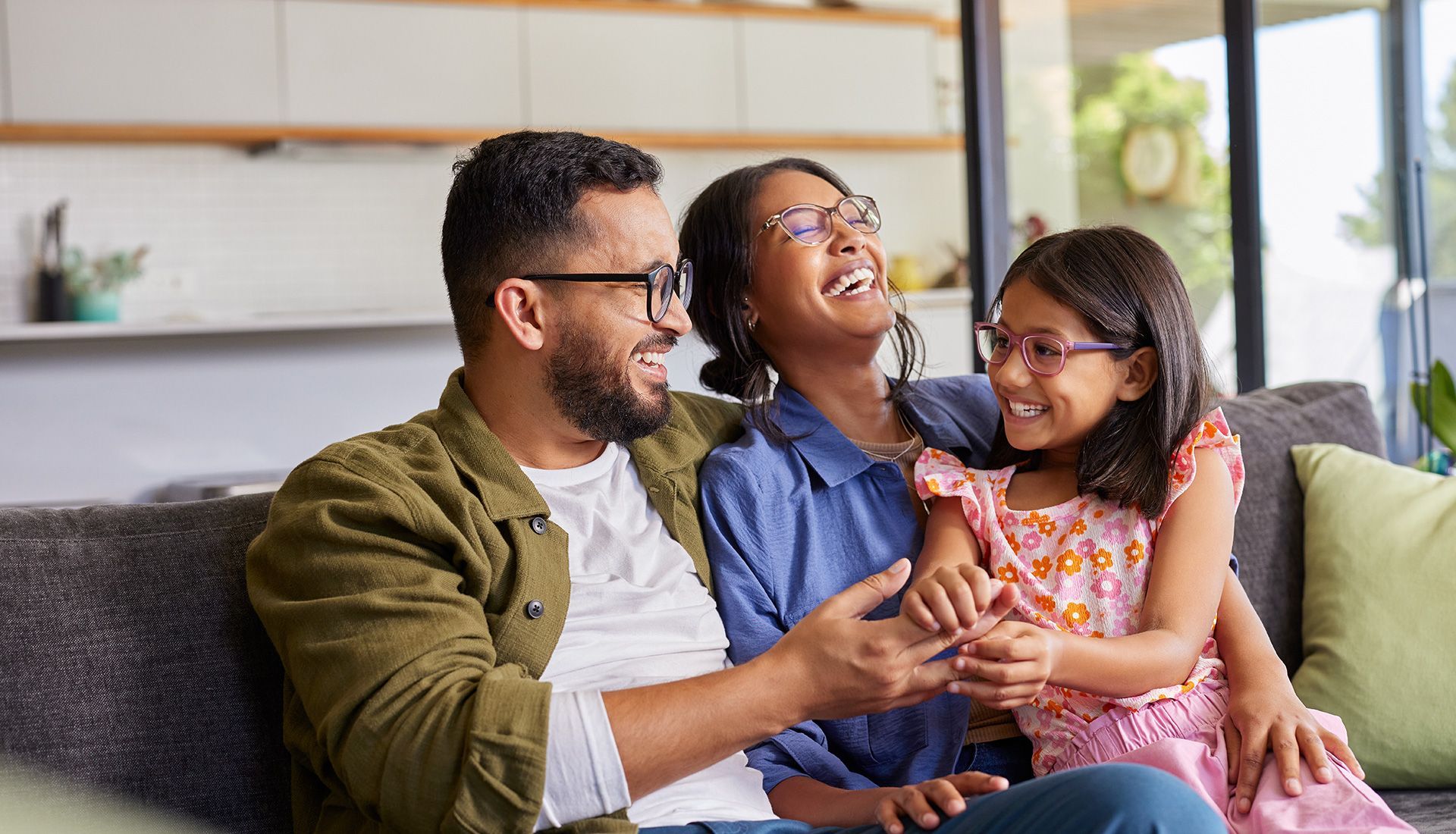 Family laughing together on a couch in a living room, with natural light.