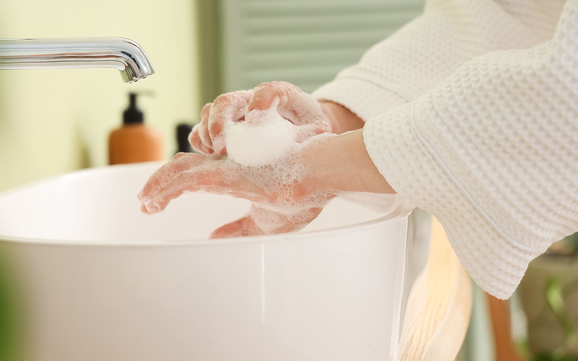 Person washing hands with soap over a white sink in a bathroom.