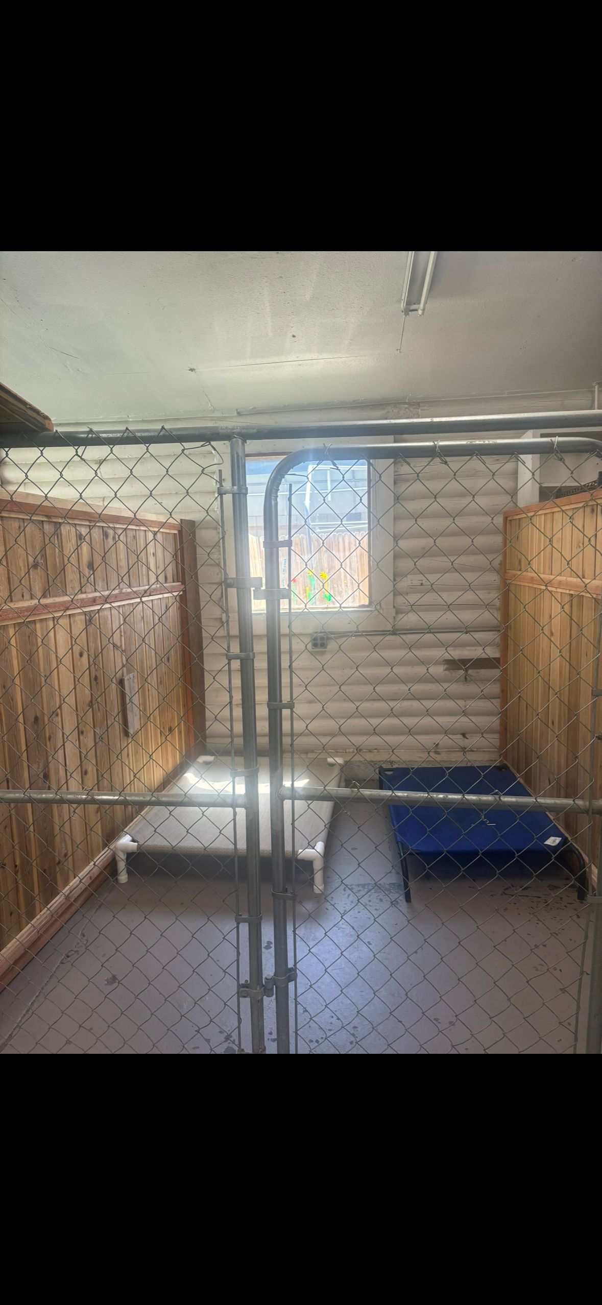 An indoor dog kennel with chain link and wooden walls. Inside are a dog bed and a blue mat.