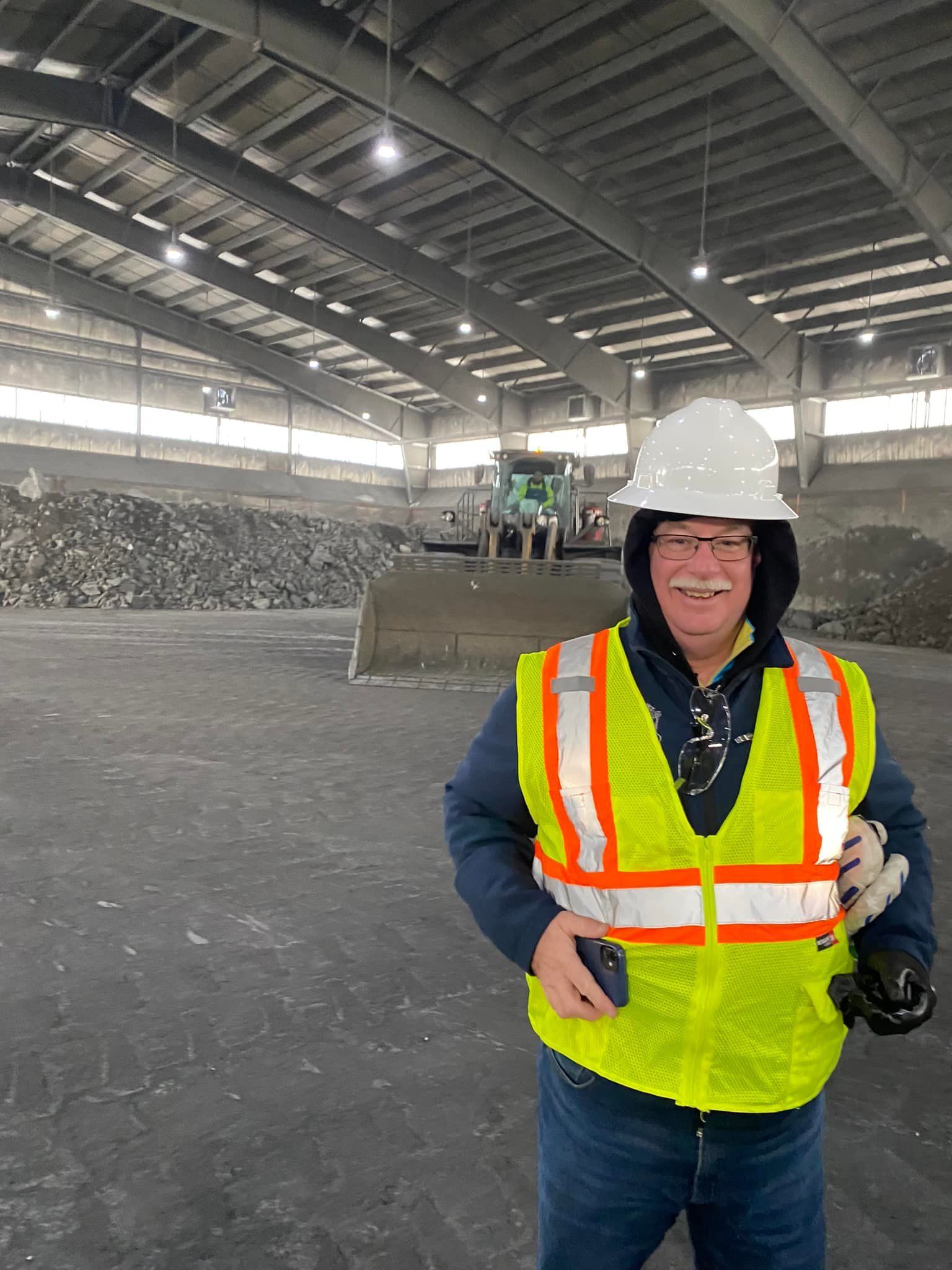 A man wearing a hard hat and safety vest is standing in a large building.