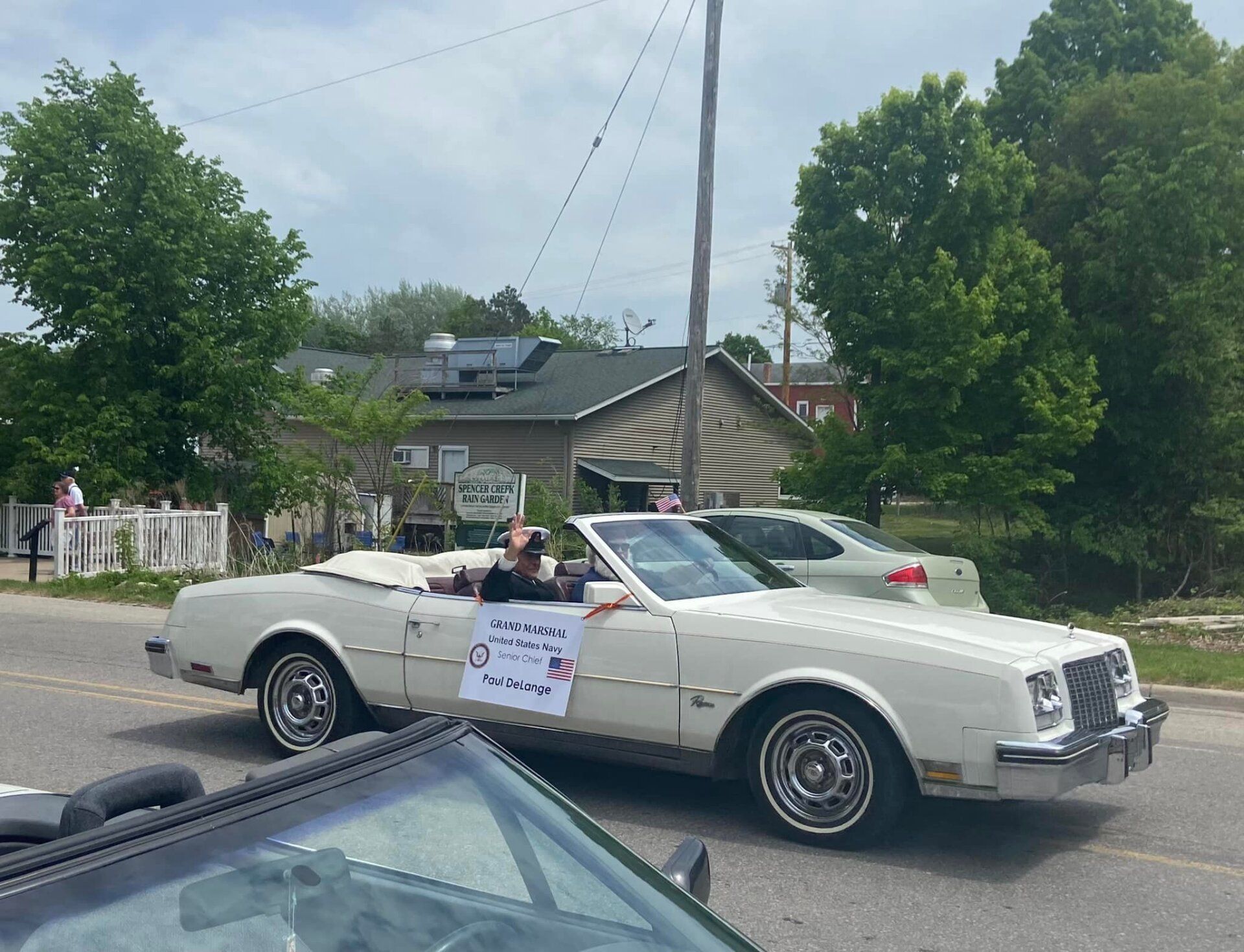 A white convertible car is driving down a street in a parade.