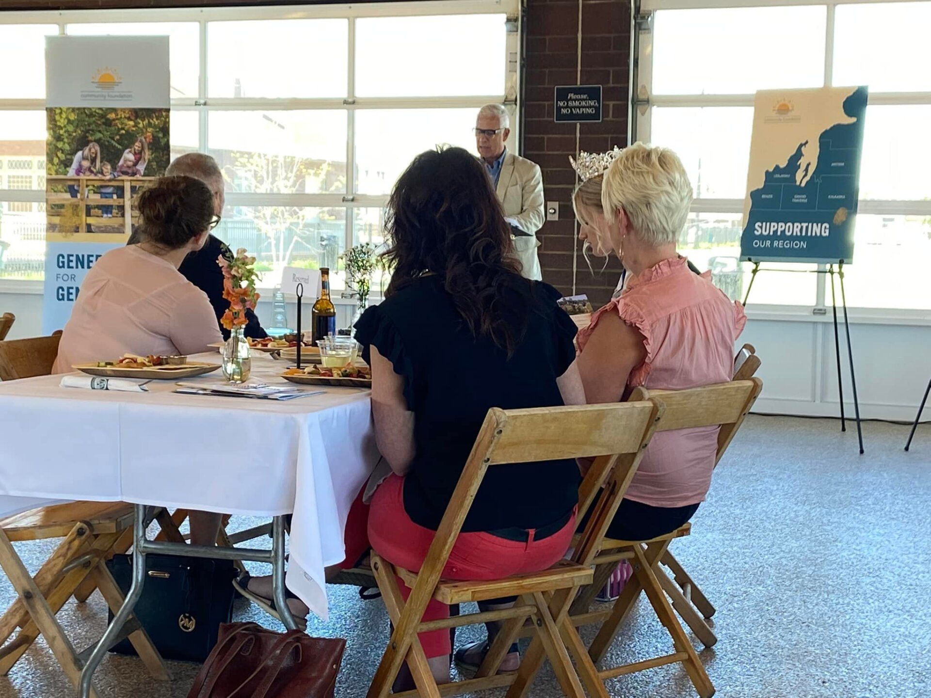 A group of women are sitting at a table with a man standing behind them.