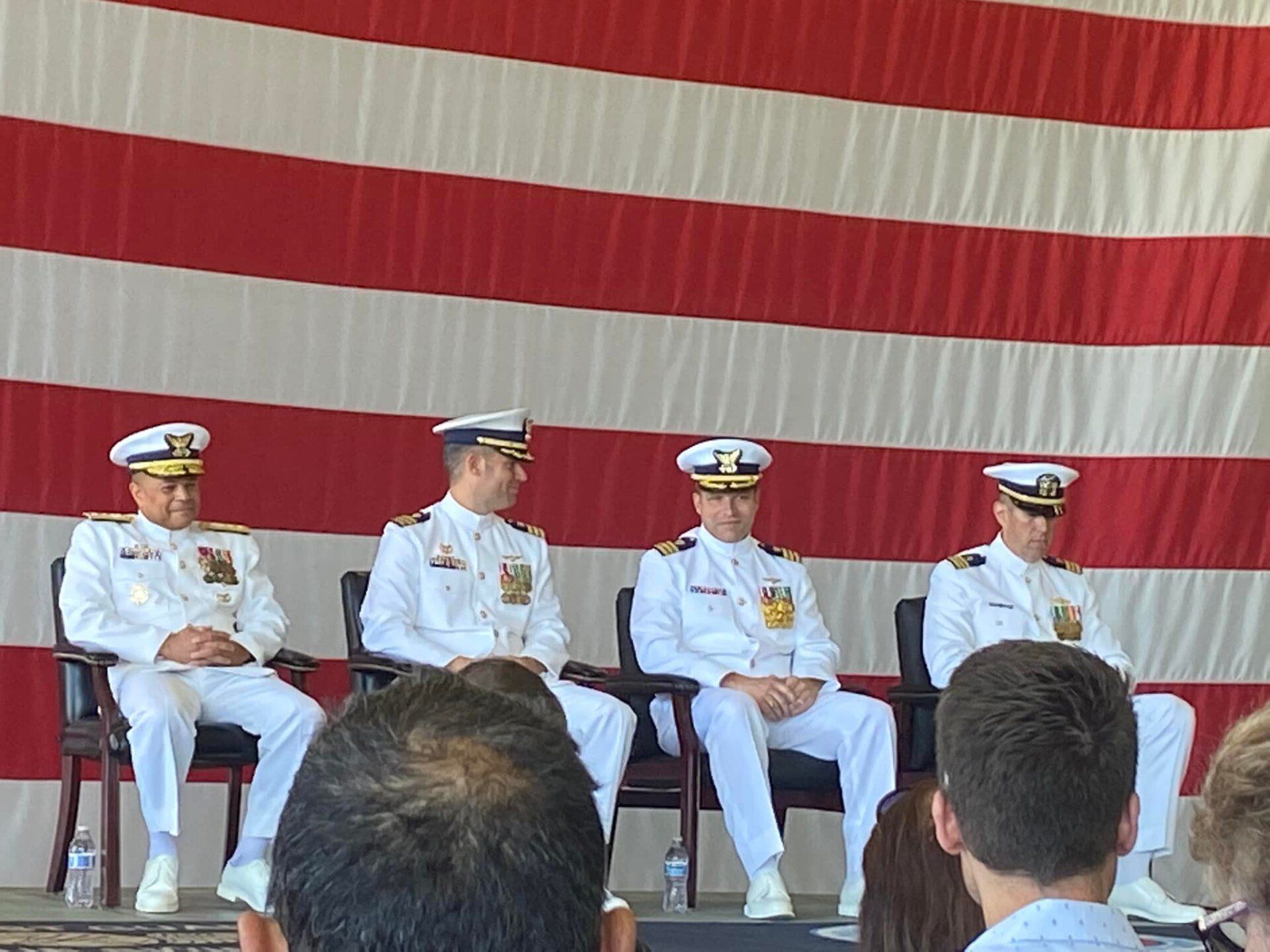 Four men in white uniforms are sitting in front of an american flag.
