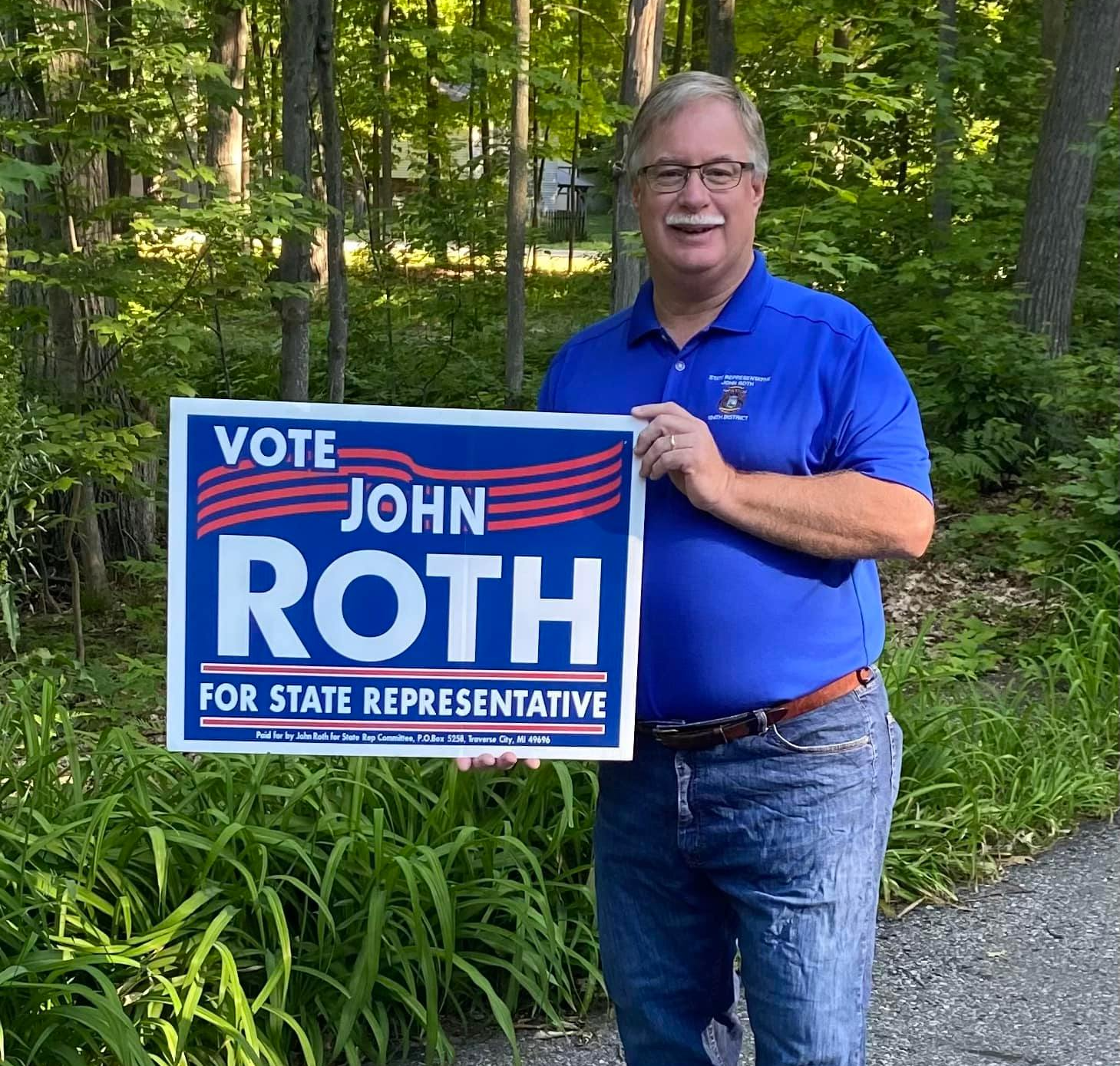 John Roth is holding a sign that says vote john roth for state representative