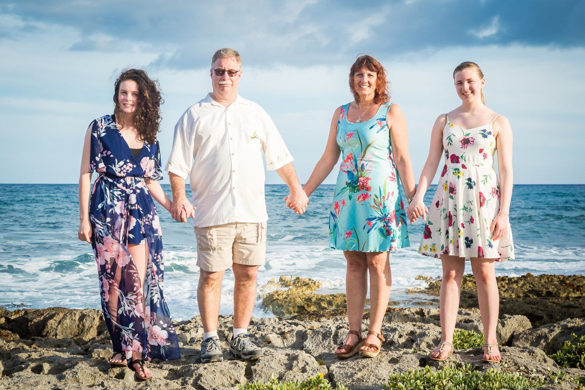 John Roth's Family  is standing on a rocky beach holding hands.