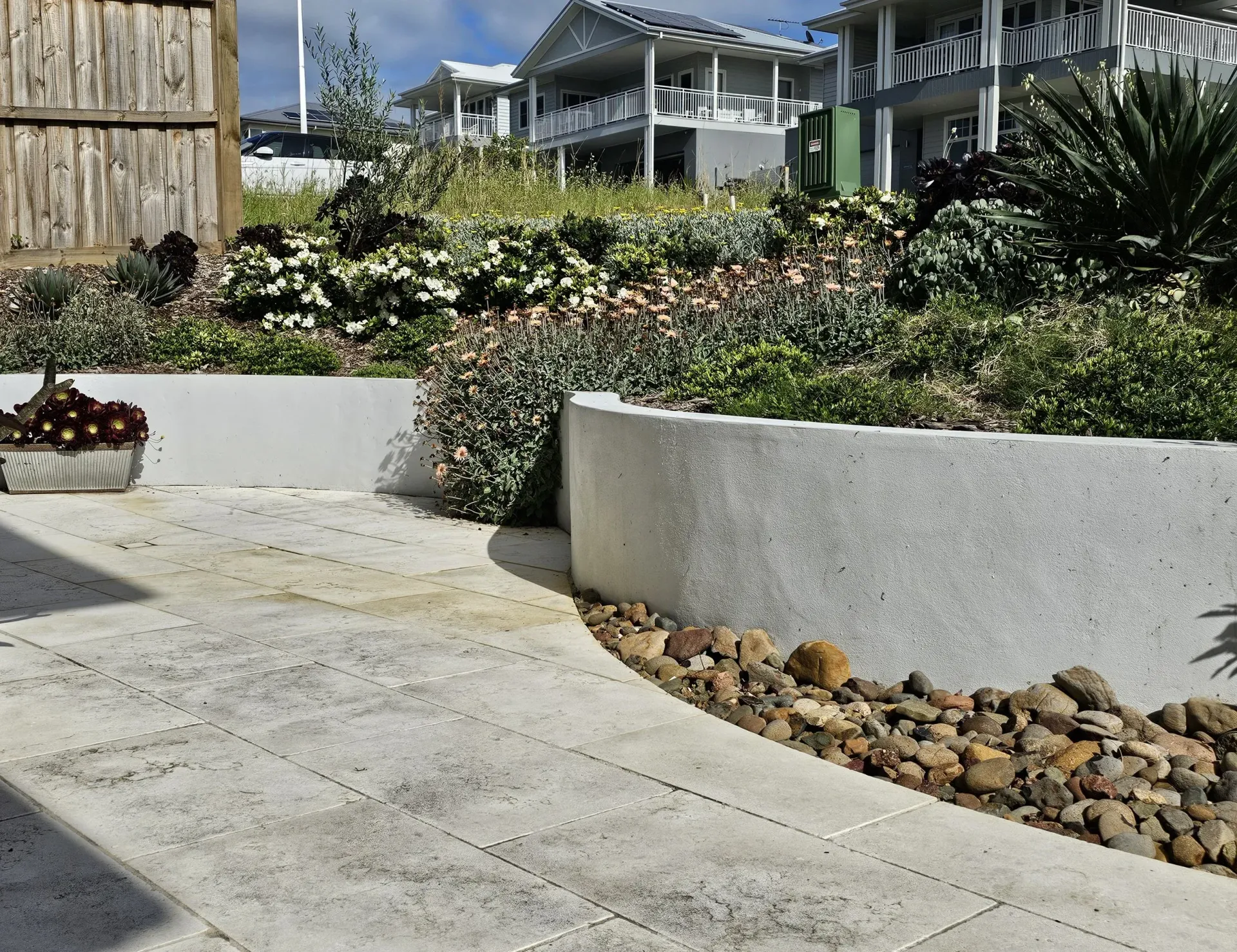 Stone patio with a white curved retaining wall and landscaped flower beds.