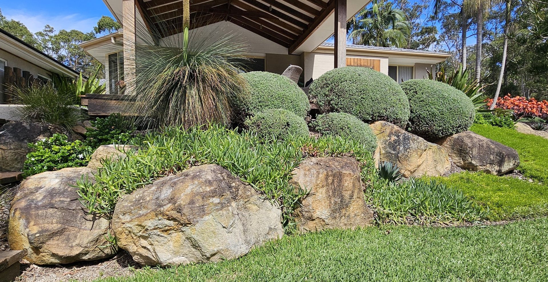 Rocks and green plants in front of a house with a covered entrance.